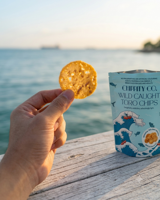 Hand holding a Toro Chip over the sea — wild-caught tuna, sea-to-shelf snack, Singapore
